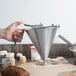 A person using a Matfer Bourgeat stainless steel confectionery funnel to frost a cupcake.