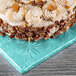 A frosted cake with pecans on a blue Enjay square cake drum.