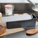 A black rectangular non-stick loaf pan with a loaf of bread and a clear lid on a counter.