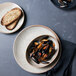 A Oneida Terra Verde Natural porcelain round coupe plate holding mussels and toast on a table.