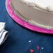 A white cake on a pink Enjay round cake drum on a table.