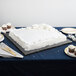 A white cake with white frosting on a black Enjay square cake drum on a table.