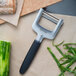 A Triangle stainless steel "Y" vegetable peeler on a cutting board next to a piece of food.