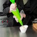 A person in gloves using a Matfer Bourgeat green plastic pastry bag to make frosting.