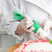 A person in white gloves using a Matfer Bourgeat disposable pastry bag to decorate a cake with green icing.