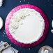 A white cake with white frosting and flowers on a pink Enjay round cake board.