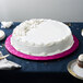 A white cake on a pink Enjay round cake board on a table.