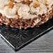 A cake with frosting and pecans on a black Enjay square cake drum.