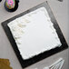 A white cake with frosting and flowers on a black Enjay Fold-Under Square Cake Drum.