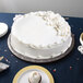 An Enjay black round cake drum under a white frosted cake on a table.