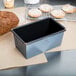 A Matfer Bourgeat steel loaf pan with a loaf of bread next to it.