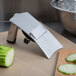 A Gefu mushroom slicer on a cutting board with a cucumber and knife.