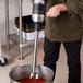 A man using a KitchenAid 400 Series immersion blender to mix liquid in a professional kitchen.