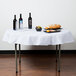 A white Intedge poly/cotton blend table cover on a table with food and wine bottles.