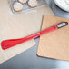 A red Matfer Bourgeat Exoglass spatula on a cutting board next to cookies.