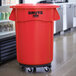 A red Rubbermaid BRUTE trash can lid with wheels.