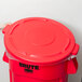 A person placing a red Rubbermaid BRUTE lid on a red trash can.