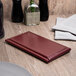 A Menu Solutions burgundy leather guest check presenter on a table.