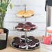 An American Metalcraft 3 tier stainless steel display stand with cupcakes and pastries on a counter.