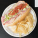 A Solo Symphony heavy weight paper plate with a sub sandwich, tomatoes, and chips on it.