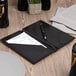 A black leather Menu Solutions guest check presenter with a pen and a receipt on a table.