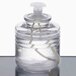 A clear glass container with a white lid filled with clear liquid.