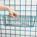 A hand holding a Metroseal 3 wire storage basket with a wire whisk inside.