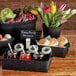 A rectangular black American Metalcraft wood basket on a table with food and flowers.
