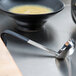 A Vollrath Jacob's Pride stainless steel ladle with a black handle serving soup in a bowl.
