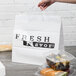 A person's hand holding a white plastic shopper bag with "Fresh Flavor" printing containing a plastic container of food.