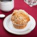 A muffin on a CAC porcelain plate on a table in a diner.