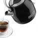 A KitchenAid onyx black electric kettle pouring tea into a glass cup.