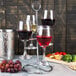 A Franmara steel wine flight holder with three wine glasses filled with red wine on a table.