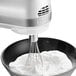 A KitchenAid white hand mixer with whisk attachment mixing whipped cream in a bowl.