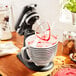 A KitchenAid black matte countertop mixer with a bowl of red liquid on top.