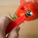 A hand with a red Prince Castle tomato corer cutting a tomato.