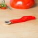 A Prince Castle tomato corer with a red plastic handle on a wood surface.
