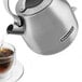 A KitchenAid brushed stainless steel electric kettle pouring tea into a glass cup.