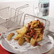 An American Metalcraft stainless steel fry basket with fries on a table.