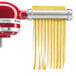 A KitchenAid pasta maker attachment with red and white parts being used.