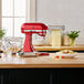 A red KitchenAid mixer on a counter with a bowl of pasta.