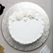 A white cake with frosting and flowers on a silver Enjay round cake board.