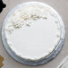 A white cake with white frosting and flowers on a silver Enjay round cake drum.