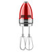 A KitchenAid candy apple red hand mixer with whisk attachment and stainless steel beaters.