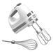 A white KitchenAid hand mixer with stainless steel attachments.
