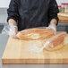 A man in a chef's uniform holding a plastic bag of French bread.