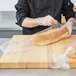 A person in a chef's uniform putting a plastic bag on a loaf of French bread.