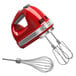 A red KitchenAid hand mixer with silver trim and a whisk attachment.