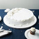 An Enjay white round cake drum under a frosted white cake on a table.