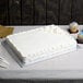 A white cake on an Enjay silver cake board on a table with cupcakes.